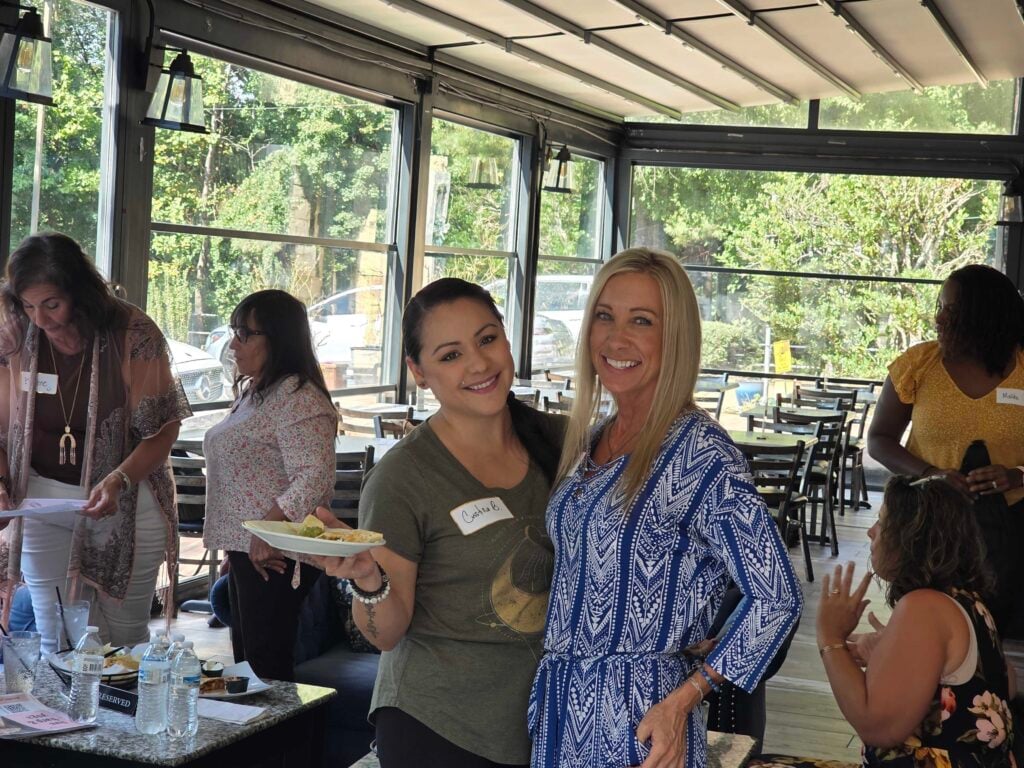 “Two women smiling together at a networking event, representing connection and community at Women’s Business Connections”