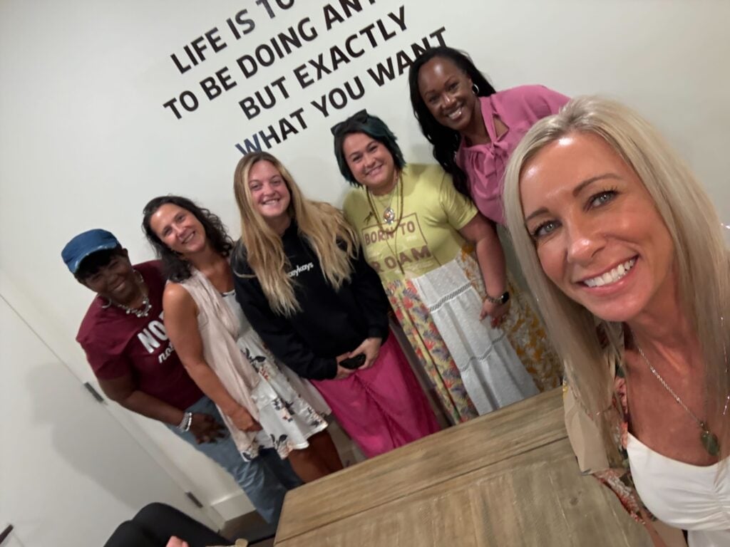 “Group of women smiling together in a meeting room, representing community, connection, and empowerment at Women’s Business Connections”