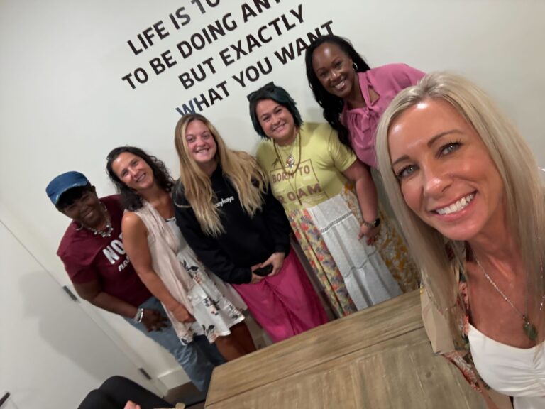 “Group of women smiling together in a meeting room, representing community, connection, and empowerment at Women’s Business Connections”